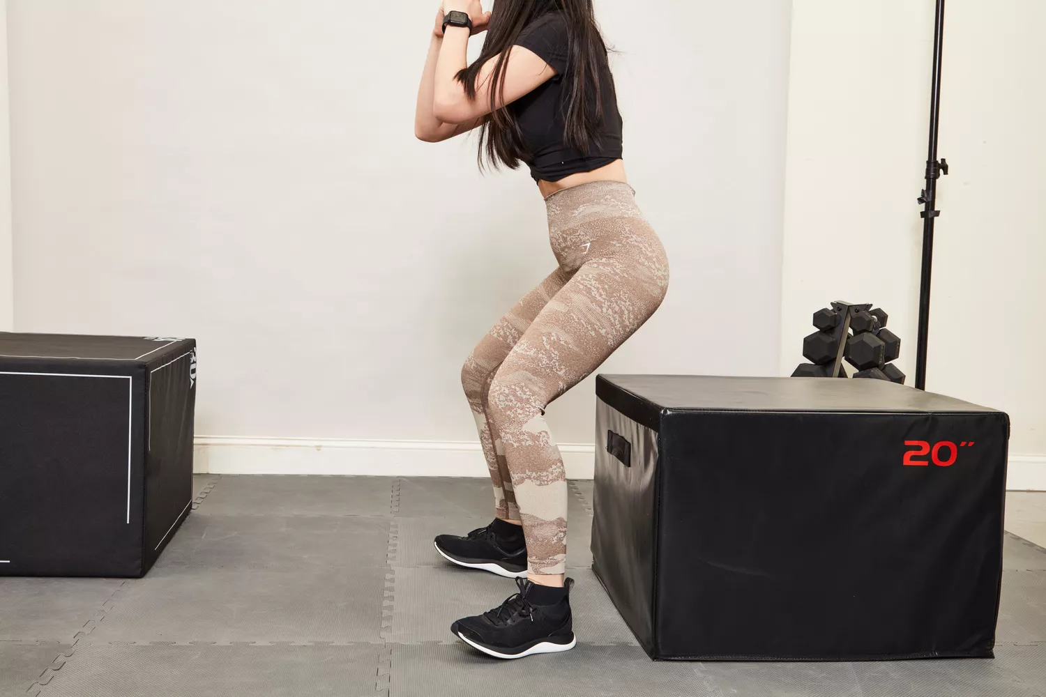 A woman in camouflage Gymshark leggings performing a box squat on a 20-inch plyo box.