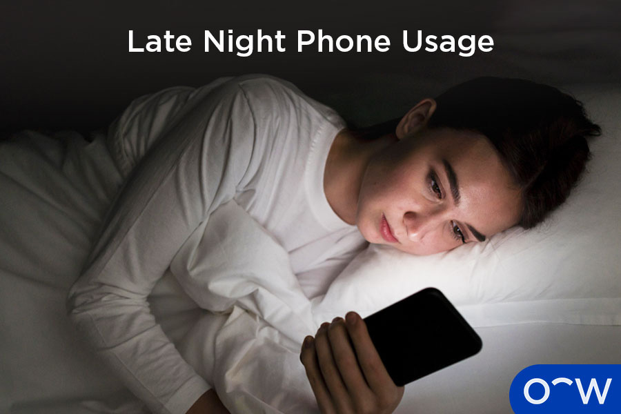 A person lying in a dark room using a bright smartphone, appearing to have eye strain.