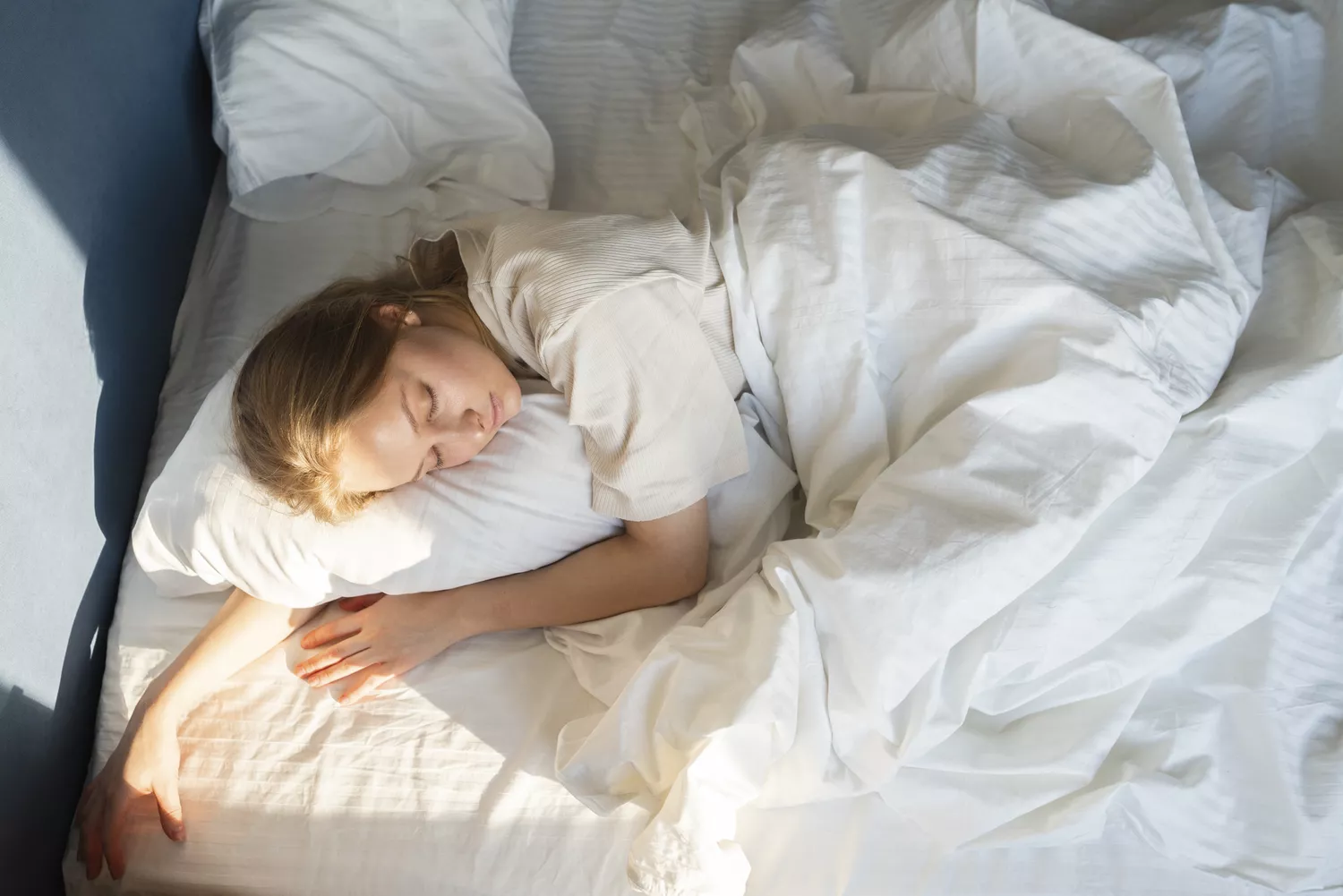 A woman sleeping peacefully in bed with soft morning sunlight on her face.