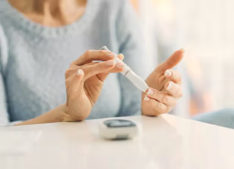 A person holding a smartphone showing a continuous glucose monitor app interface next to a beverage.