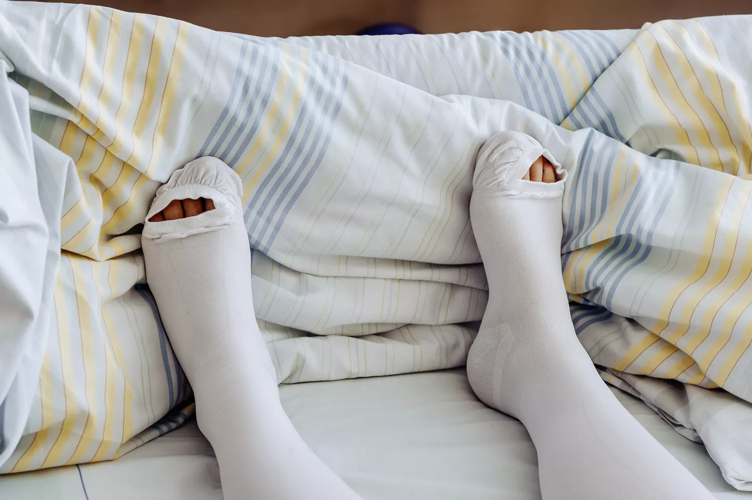 A person wearing white medical compression stockings while seated.