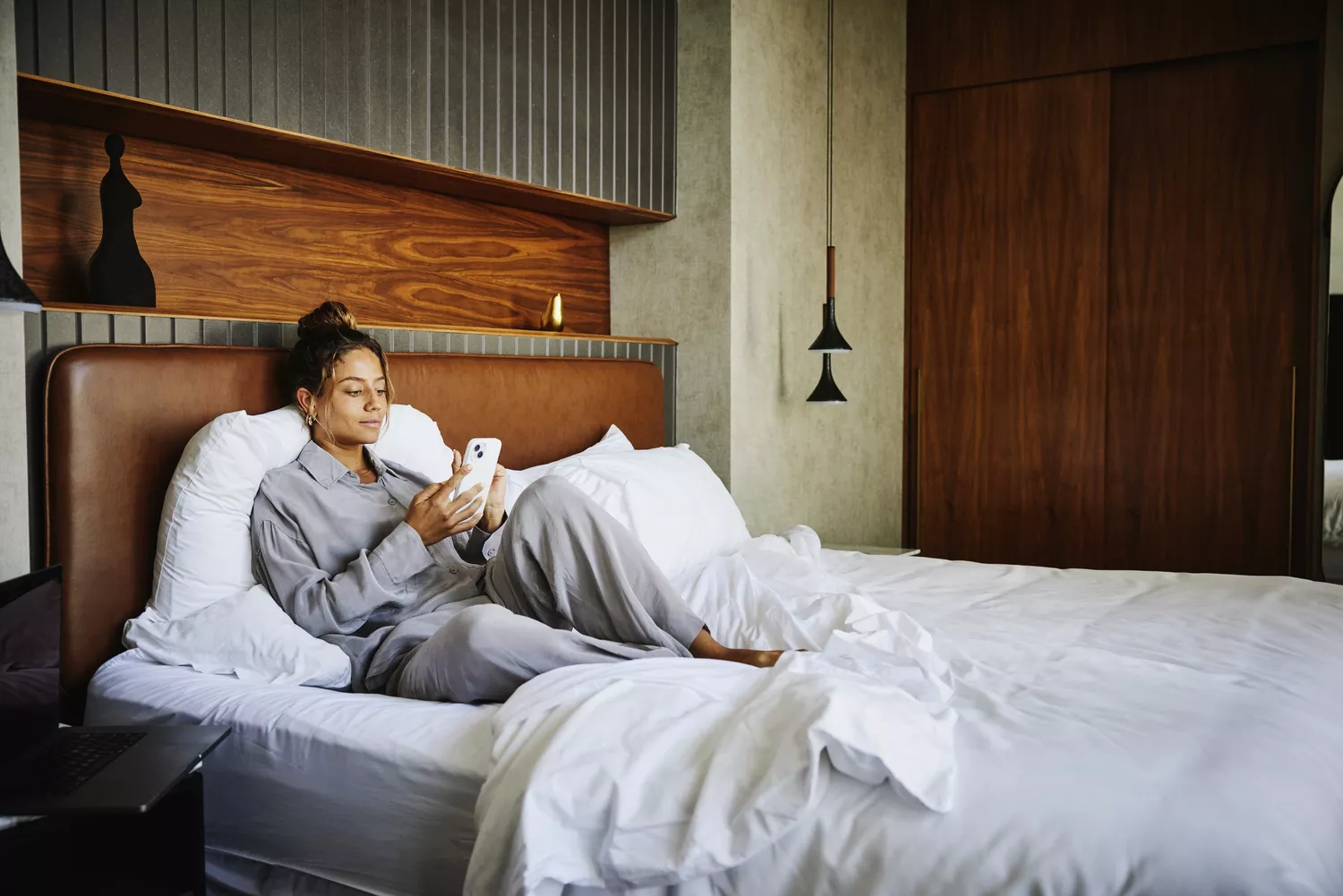 A woman lying in bed in a dark room, illuminated by the blue light of her smartphone screen.