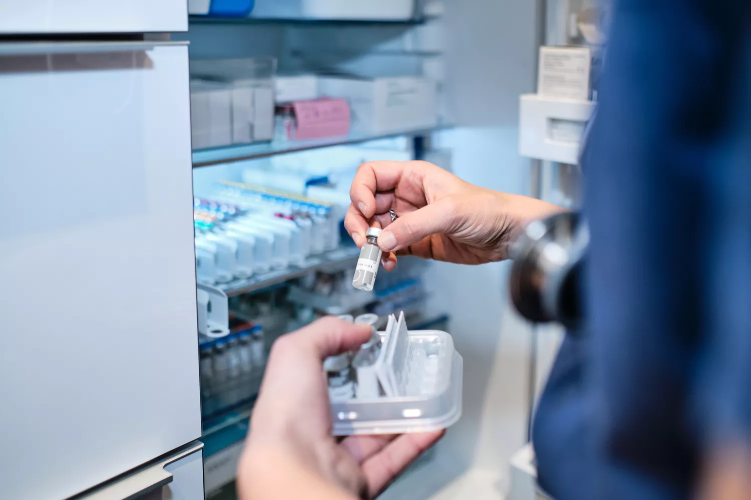 A healthcare professional in a white coat retrieving a medication vial from a professional refrigerator.