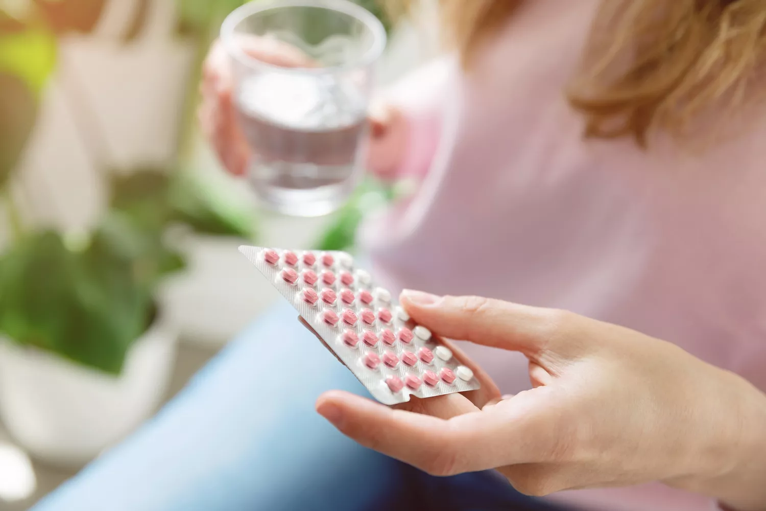 Woman holding a blister pack of pills and a glass of water.
