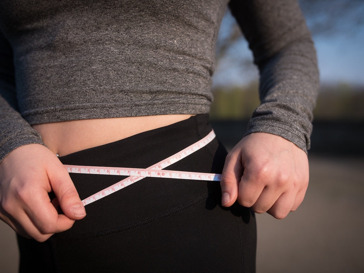 A woman measuring her waist with a yellow tape measure.