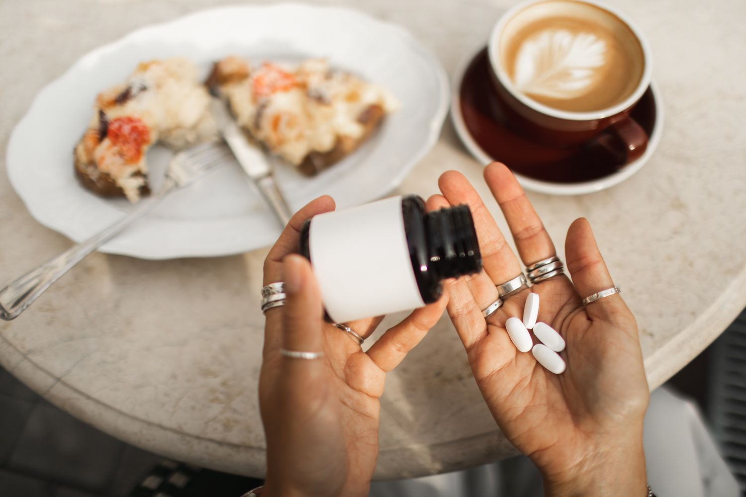 A person pouring supplement pills into their hand next to a meal