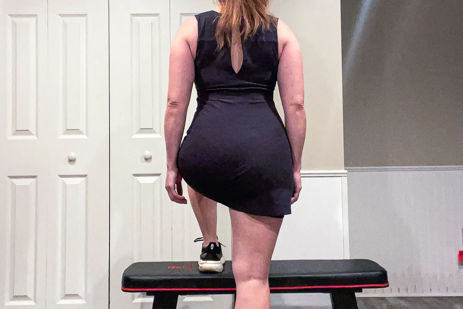 A person performing a dynamic fitness movement while wearing a black Girlfriend Collective mini dress.